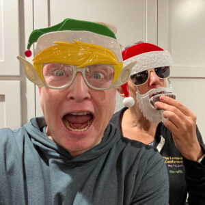 Kat and I with Christmas masks. Kat is eating a cookie. It's 2021.