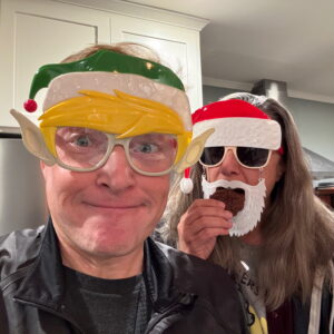 Kat and I with Christmas masks. Kat is eating a cookie. It's 2023.