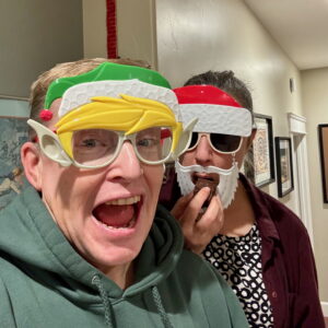 Kat and I with Christmas masks. Kat is eating a cookie. It's 2024.