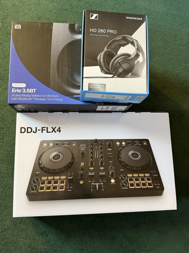 Three boxes on the floor. A Pioneer DDJ-FLX4, headphones, and a pair of monitor speakers.